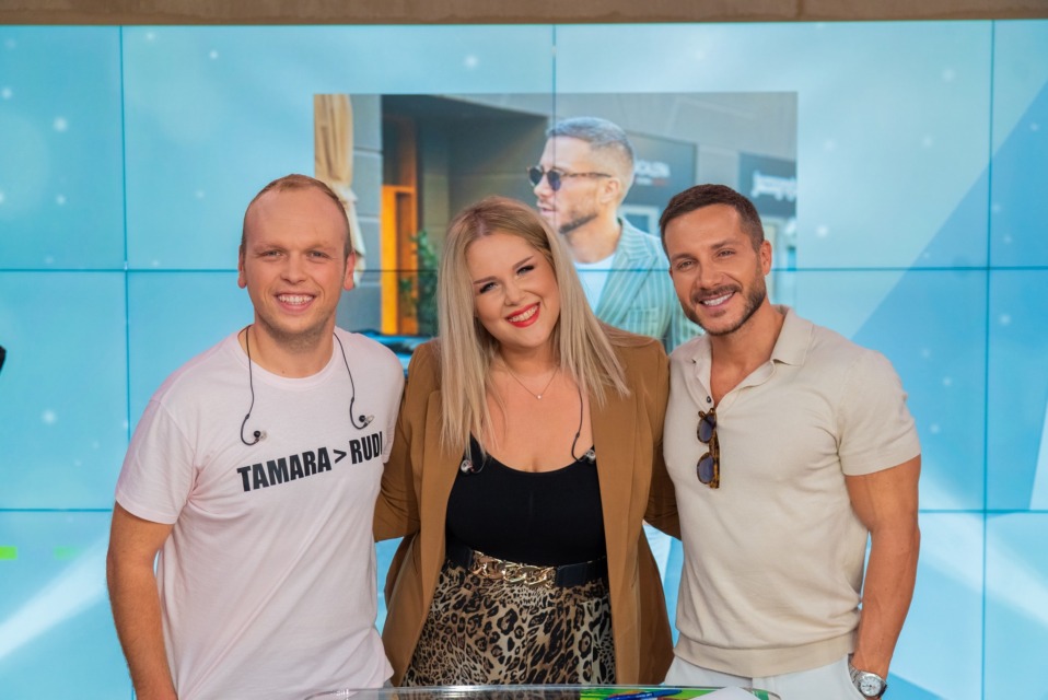 Three adults posing and smiling in front of a blue wall backdrop.