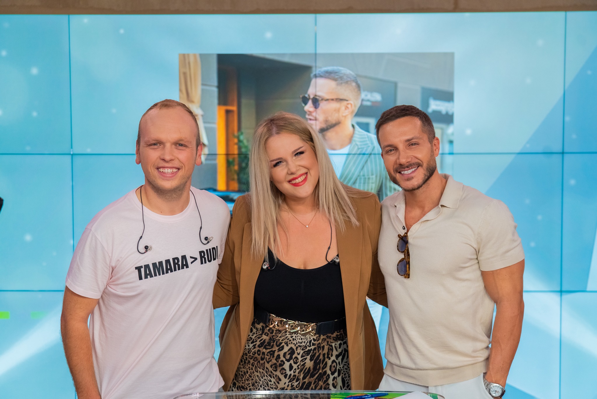 Three adults posing and smiling in front of a blue wall backdrop.