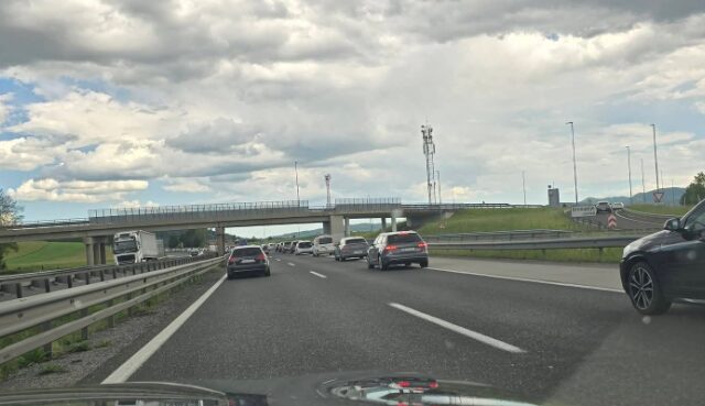 Highway scene with several cars driving on a multi-lane road beneath an overpass on a cloudy day.