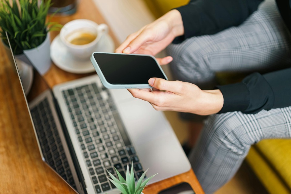 Oseba, ki ob kavi uporablja prenosnik in telefon