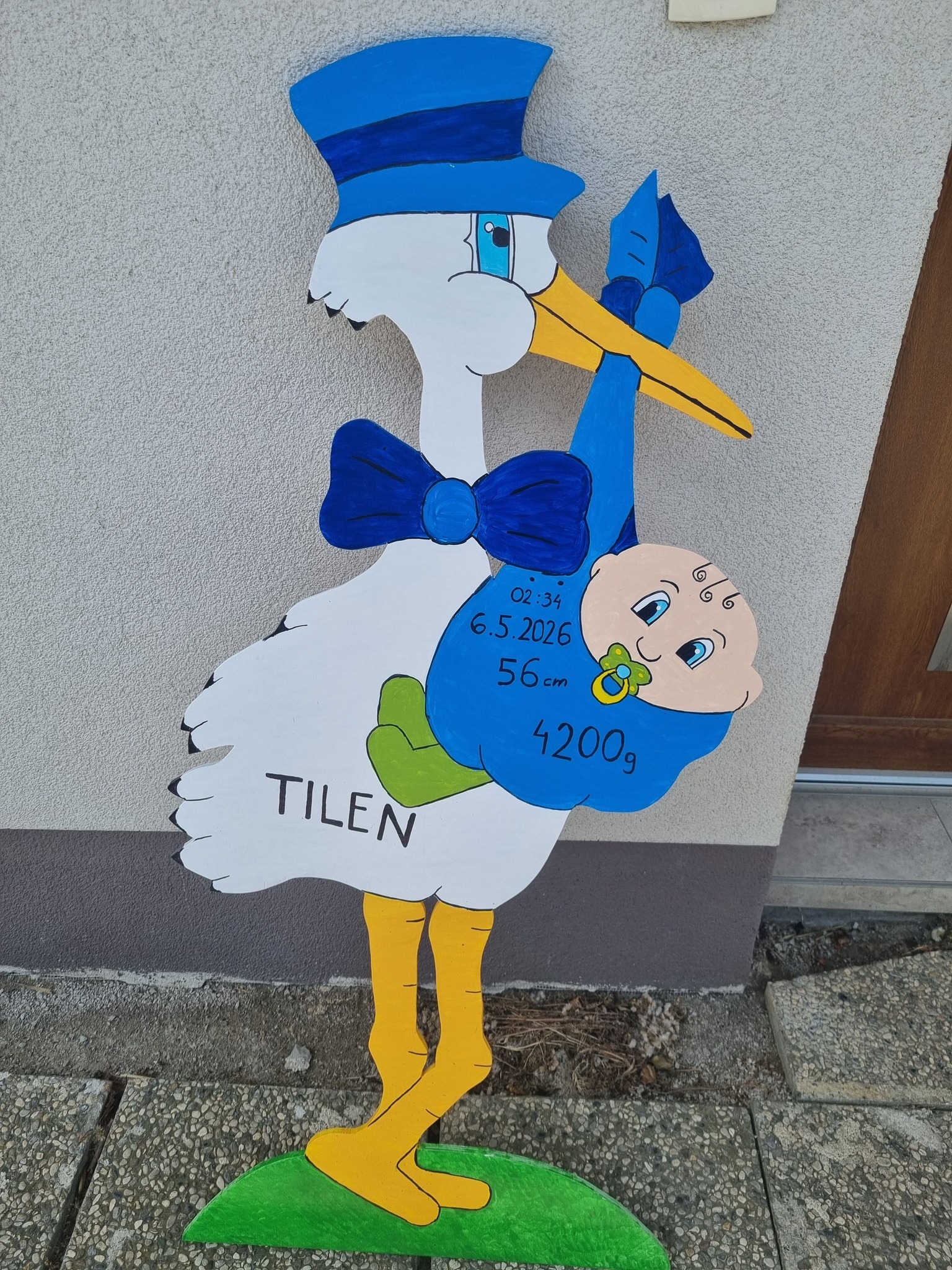 Decorative baby-announcement cutout showing a blue-styled stork carrying a baby, with birth details written on the blue body (date, weight, length).
