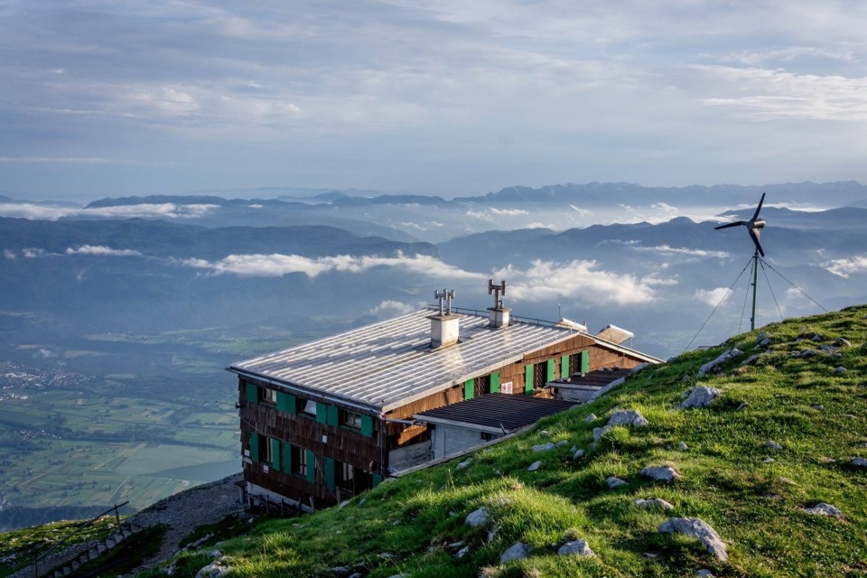 Prešernova koča na Stolu z razgledom na okoliške gore in dolino.