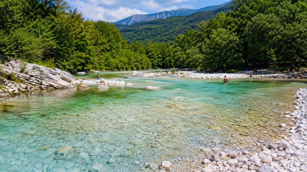 Naravno kopališče ob reki Nadiži s plitvo turkizno vodo, prodnatim bregom in zelenimi gozdovi.