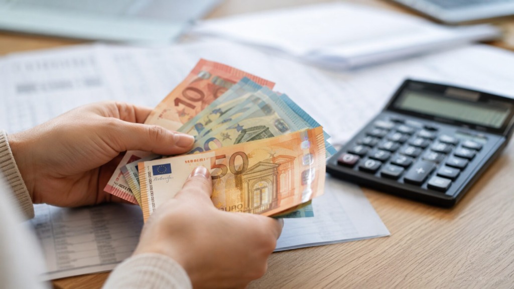 Roke štejejo evrske bankovce ob kalkulatorju pri izračunu neto minimalne plače.