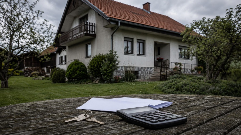 Podedovana družinska hiša s ključi, dokumenti in kalkulatorjem v ospredju.