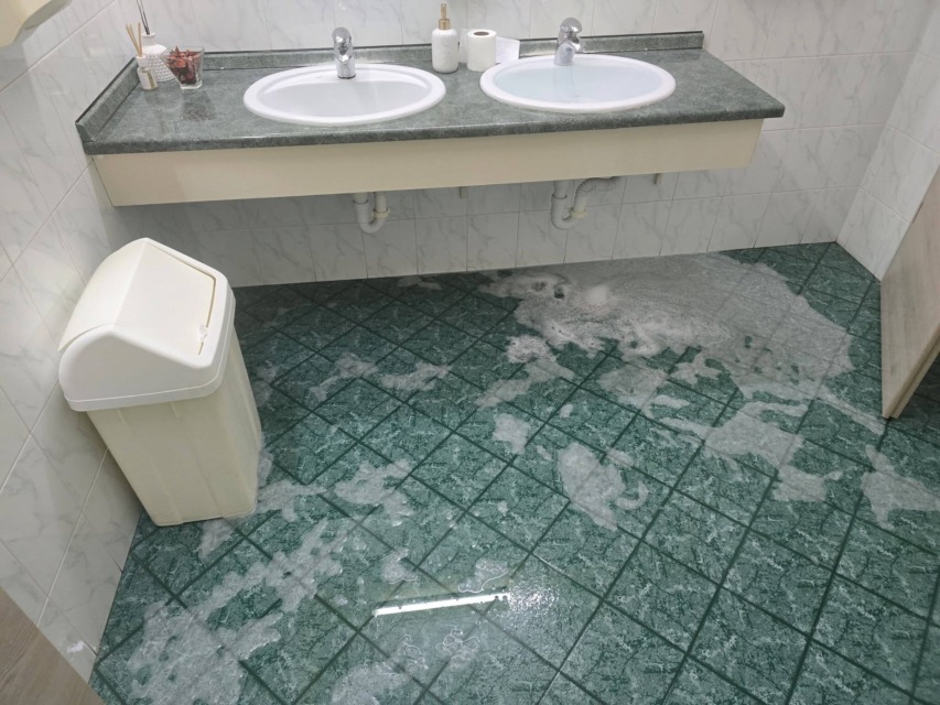 Poplavljeno žensko stranišče v Hiši Primc, kjer se je po tleh razlila voda z milnico.
